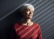 An older woman with white hair standing against a wall