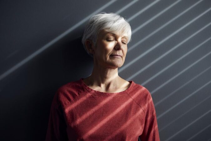 An older woman with white hair standing against a wall