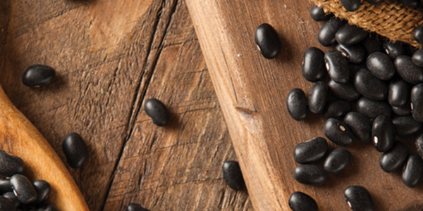 A wooden spoon filled with black beans on top of a table