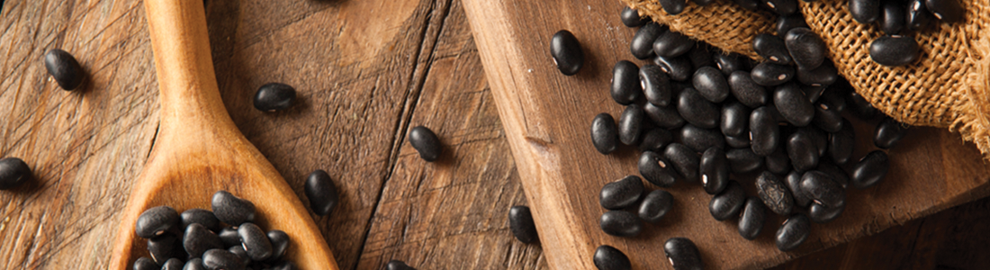 A wooden spoon filled with black beans on top of a table