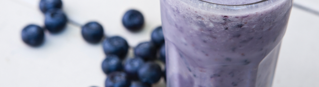 A blueberry smoothie in a tall glass next to blueberries