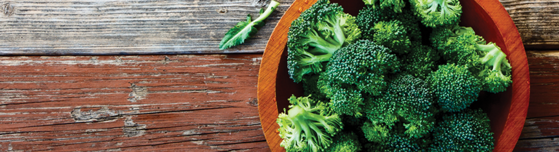 A wooden bowl filled with broccoli on top of a wooden table