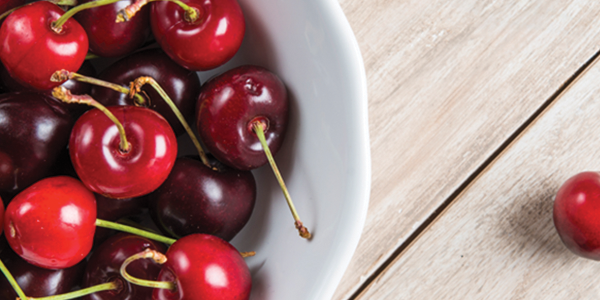 cherries A white bowl filled with cherries on top of a wooden table