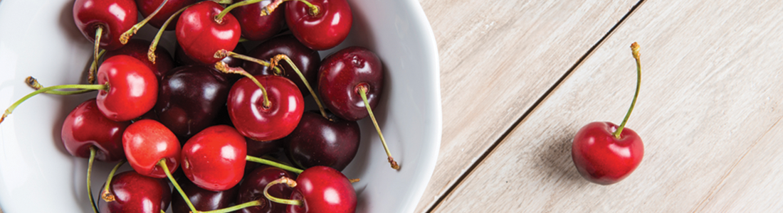 A white bowl filled with cherries on top of a wooden table