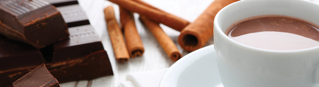 A cup of hot chocolate next to some cinnamon sticks