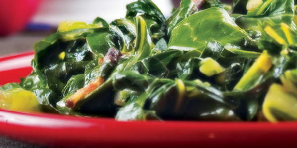 A red bowl filled with greens on top of a table