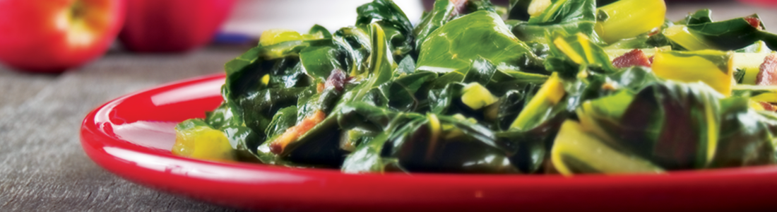 A red bowl filled with greens on top of a table