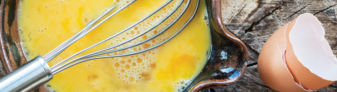 A bowl with eggs and a whisk on a wooden table