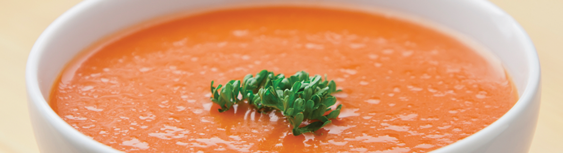 A bowl of carrot soup with a sprig of parsley