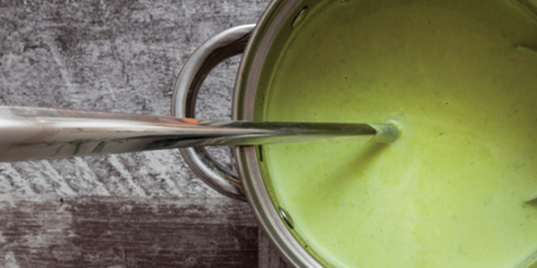 A spoon sticking out of a green sauce in a pot