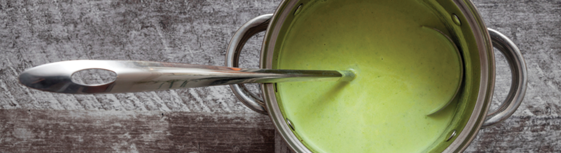 A spoon sticking out of a green sauce in a pot