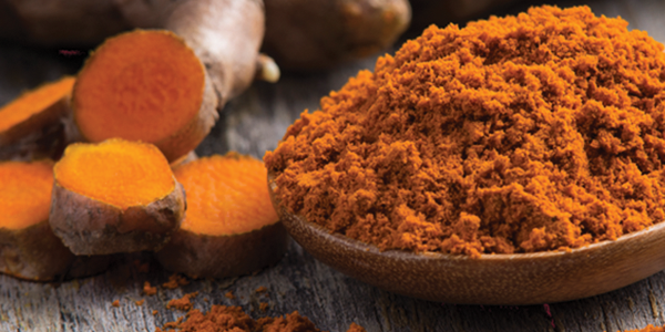 A wooden spoon filled with tumerical and ginger