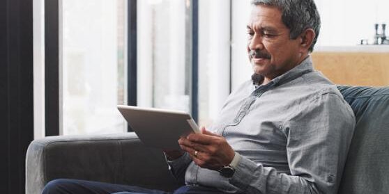 gettyimages-1283630028-170667a_0 A man sitting on a couch looking at a tablet