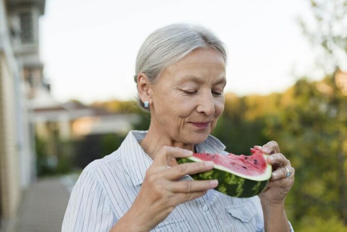 An older woman eating a piece of watermelon