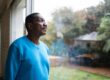 A man in a blue sweater looking out a window