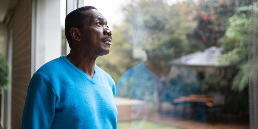 A man in a blue sweater looking out a window