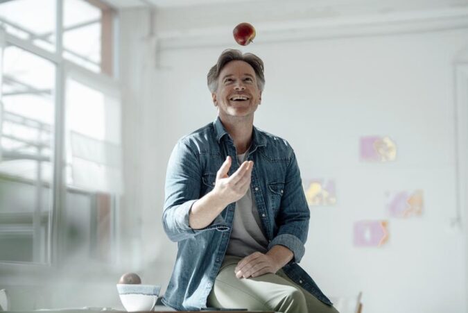 A man sitting on top of a table with an apple on top of his head