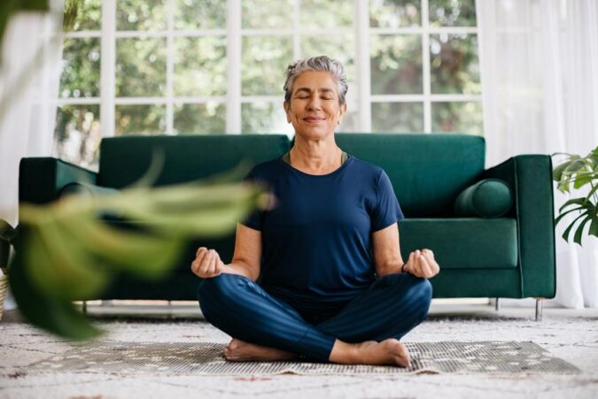 A woman sitting in a lotus position in front of a green couch
