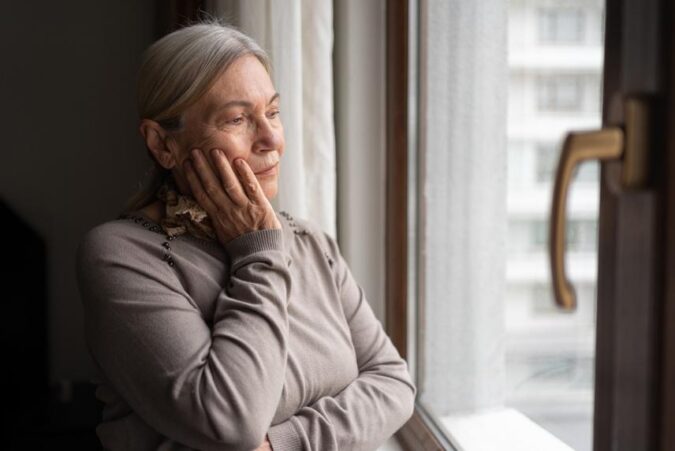 A woman looking out a window with her hands on her face