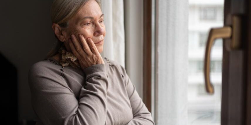 A woman looking out a window with her hands on her face