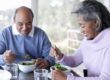 A man and woman sitting at a table eating salad
