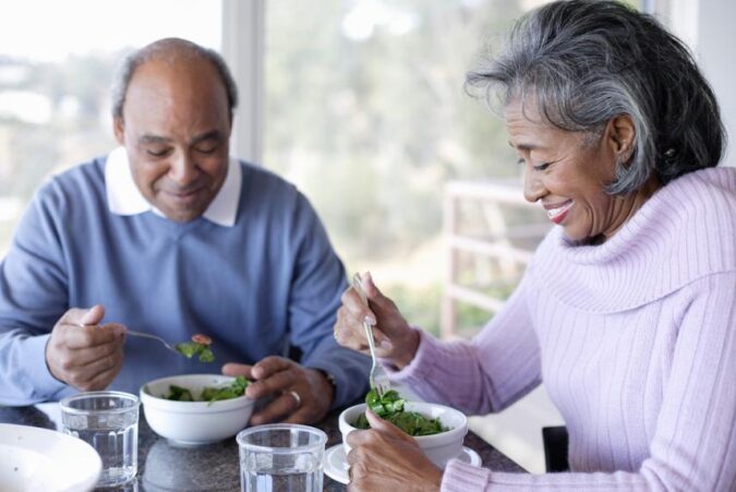 A man and woman sitting at a table eating salad